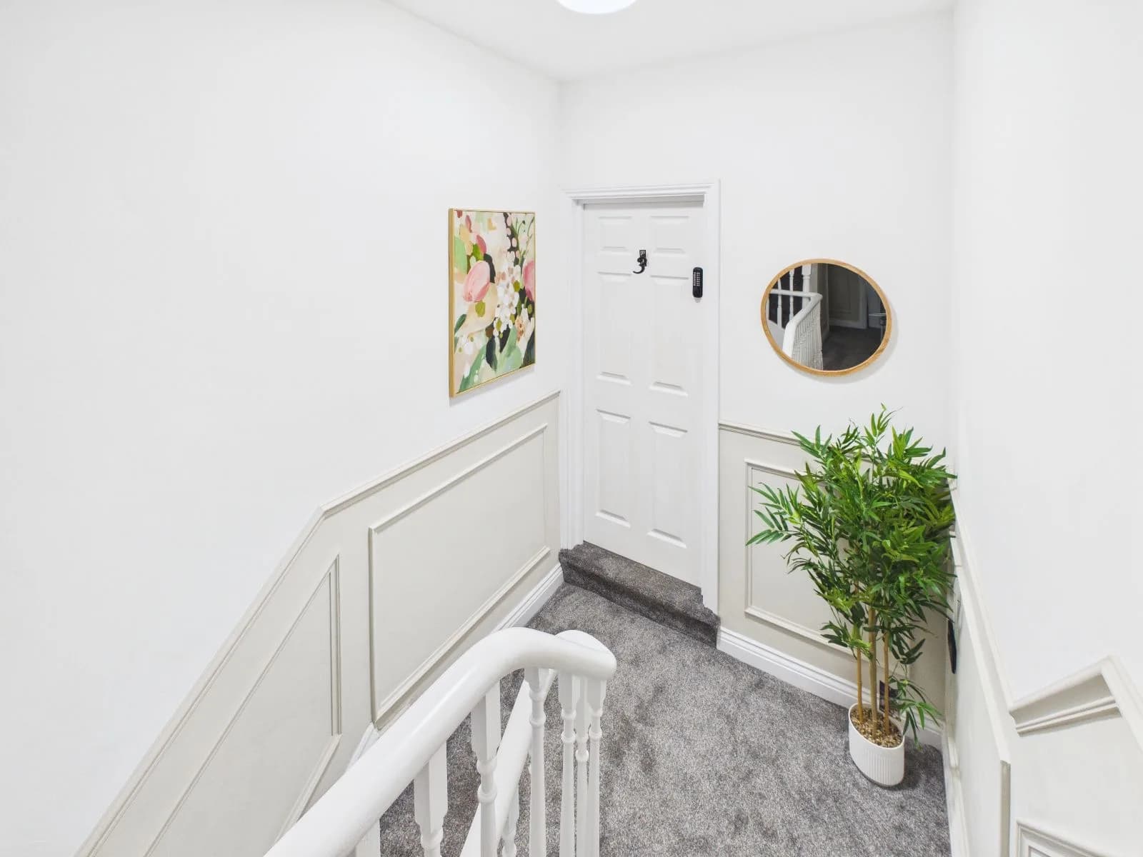 Landing and stair with panelled walls, a round mirror and a plant at the completed Darlington HMO.